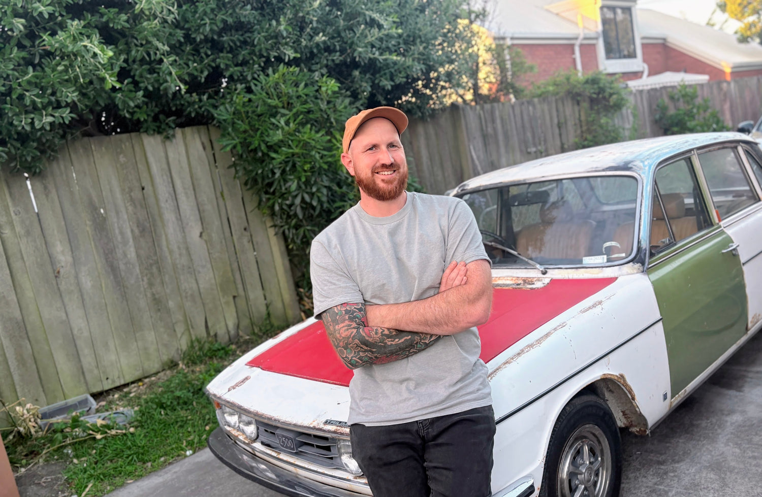 Simon standing in front of a vintage car with a wooden fence and trees in the background