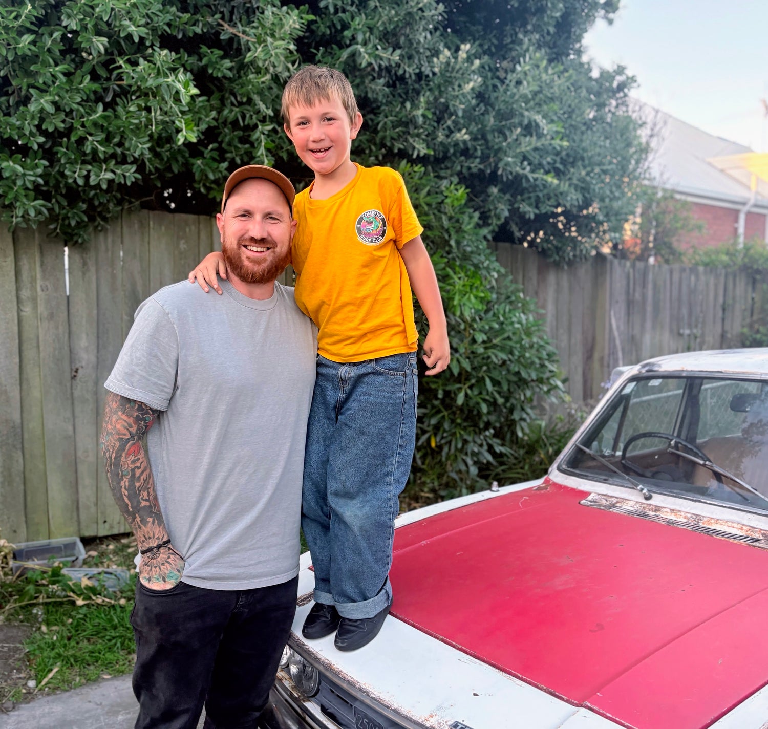 Simon and Max standing on a classic car in a backyard setting